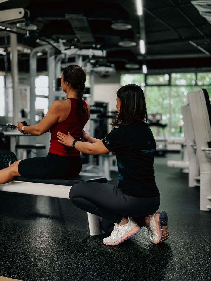 A personal trainer helps a woman with her exercise routine in a modern gym environment.